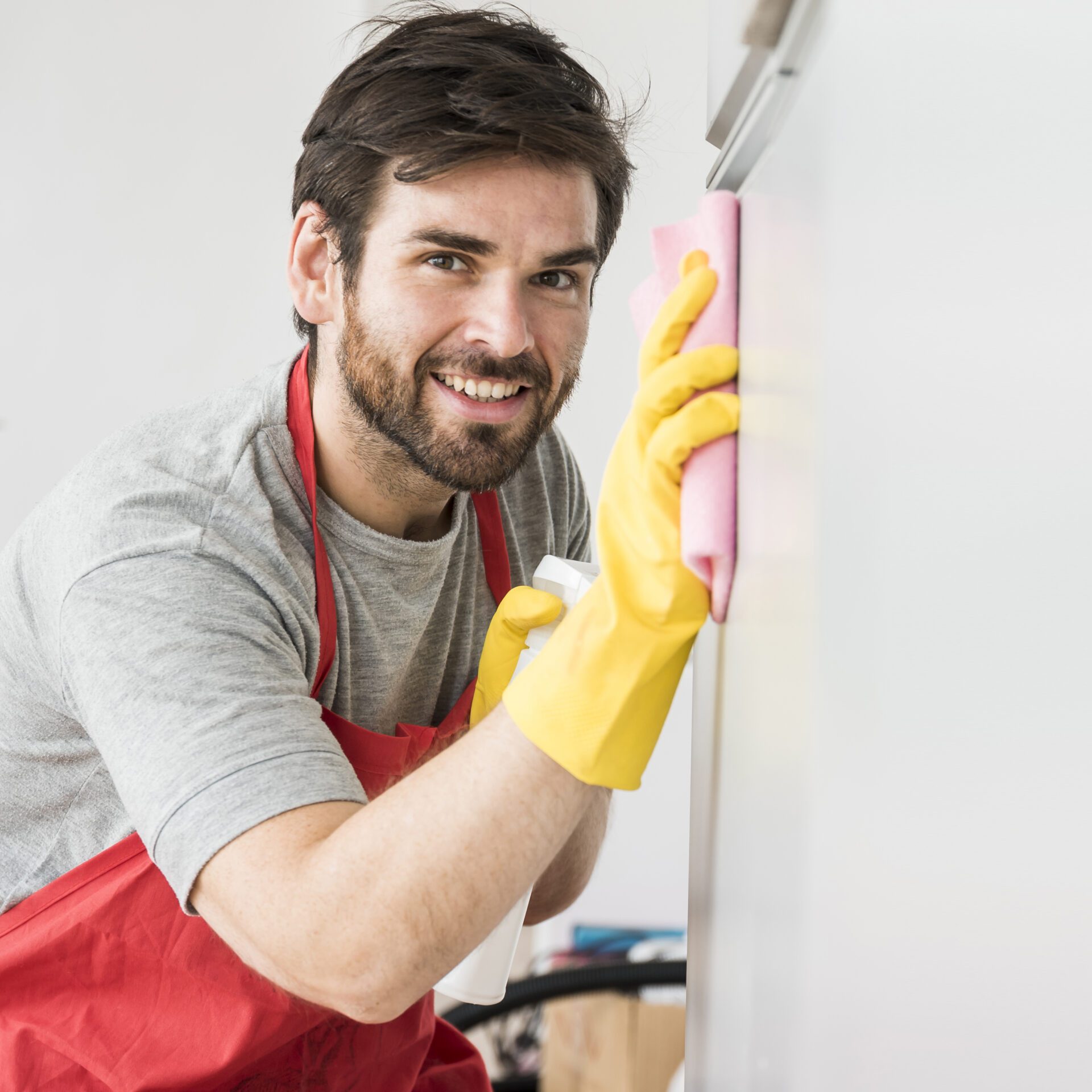 A man wearing rubber gloves and an apron diligently cleans a refrigerator, maintaining cleanliness and organization